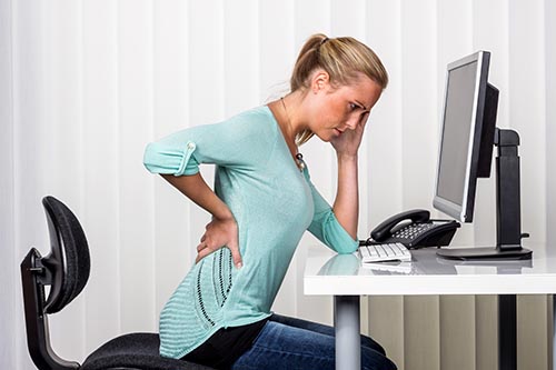 Frau sitzt am Arbeitsplatz und hat Rückenschmerzen